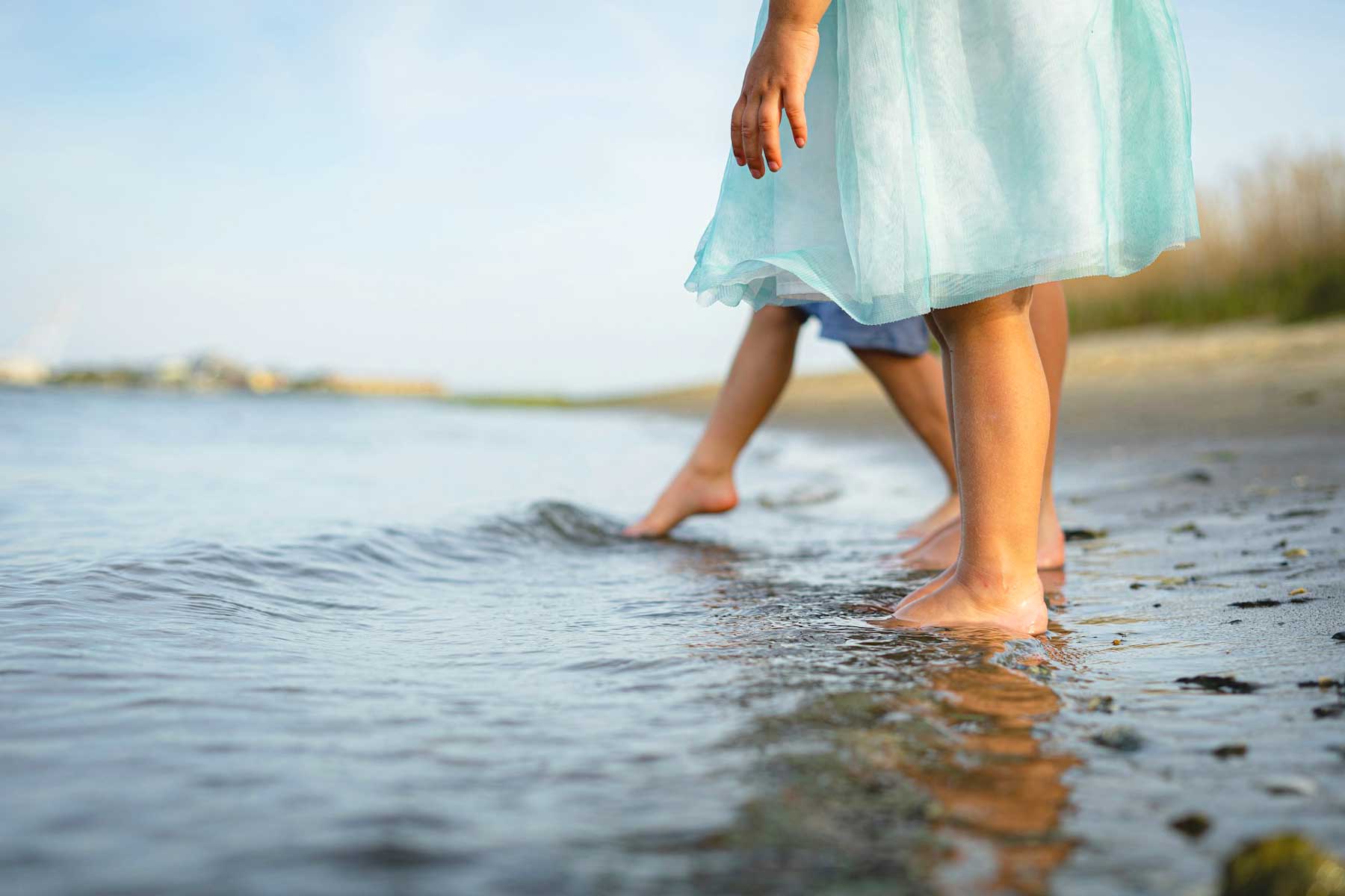 Unterstützung für Jugendliche nach belastenden Erfahrungen Mädchen im blauen Kleid läuft barfuß am Wasser entlang – Sinnbild für neue Wege nach Krisen und Trauer