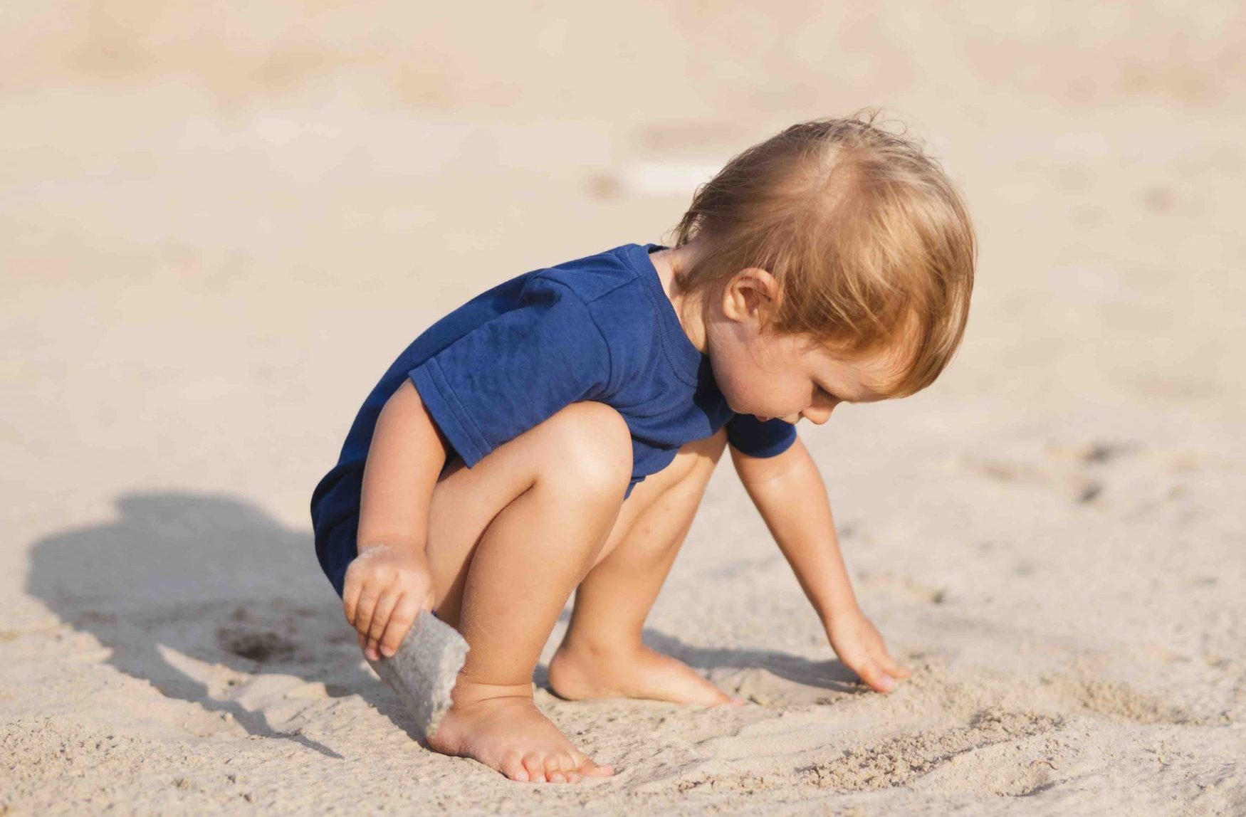 Traumasensible Begleitung für Kleinkinder in Dresden Kleinkind hockt am Strand und spielt im Sand – Symbol für Geborgenheit und sicheren Entwicklungsraum