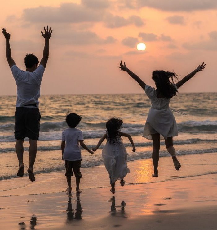 Zwei Kinder, zwei Erwachsene am Strand bei Sonnenuntergang. Gemeinsam springen sie in die Luft.